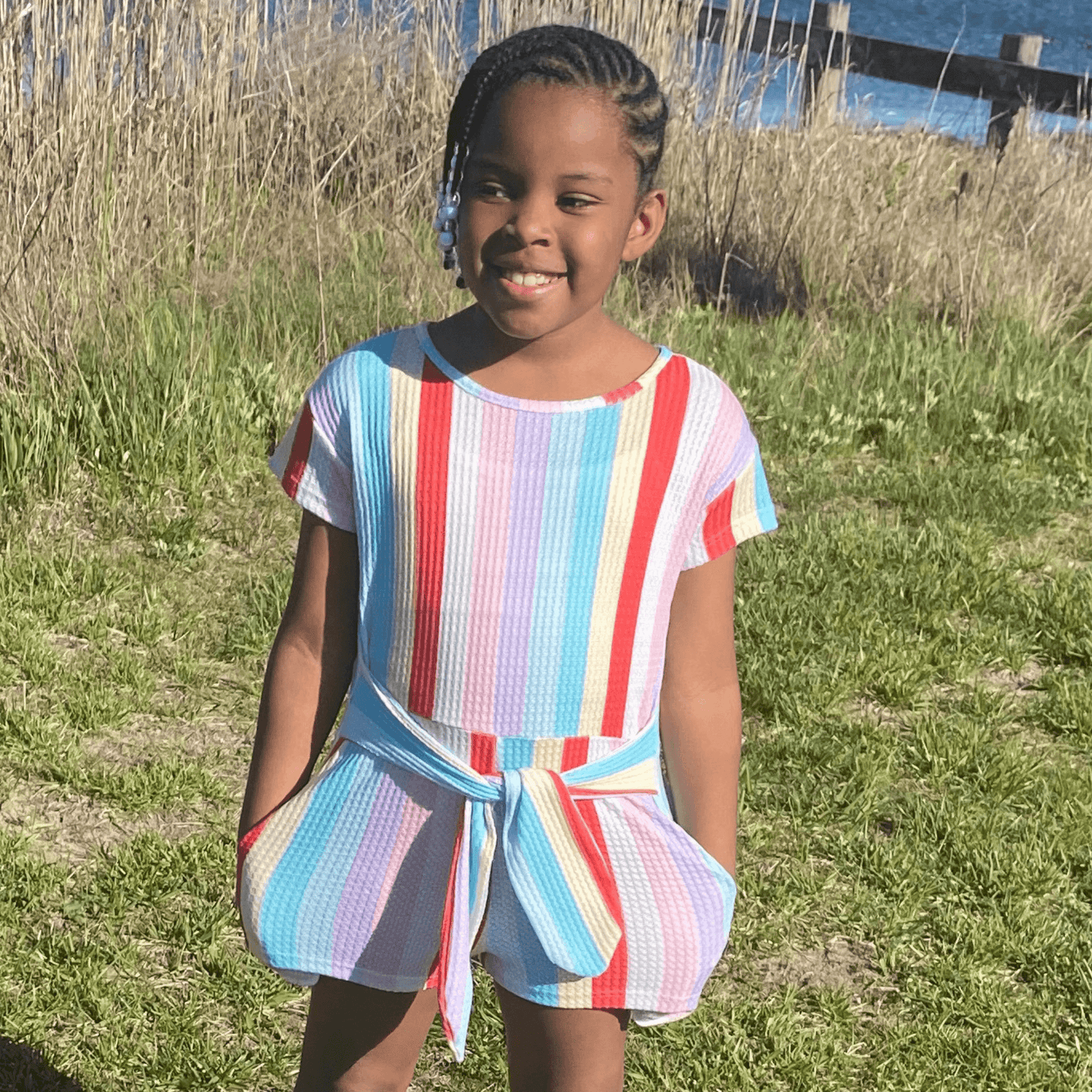 It's time to play in this striped waffle romper featuring a waist tie and pockets. This comfortable romper is perfect for playtime or a day on the town!