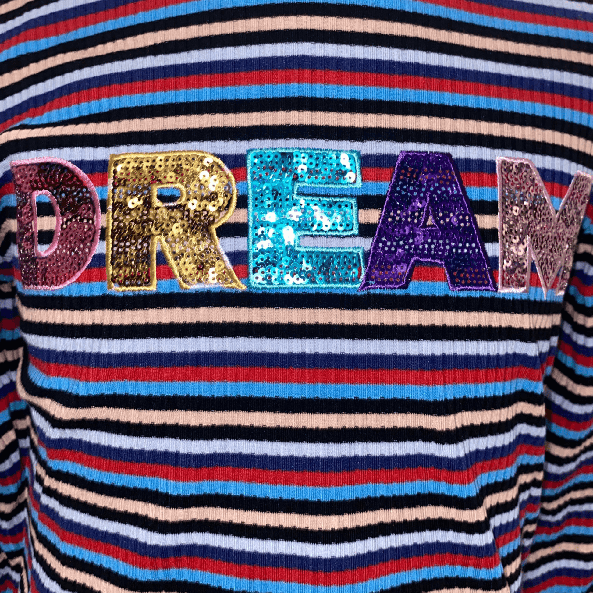 Our ruffle sleeved "DREAM" shirt is a perfect addition to the wardrobe of the little lady in your life.  This shirt features long sleeves and a mock turtle neck with scalloped edges.  This shirt has red, navy, and blue stripes with the word "DREAM" in sequins.