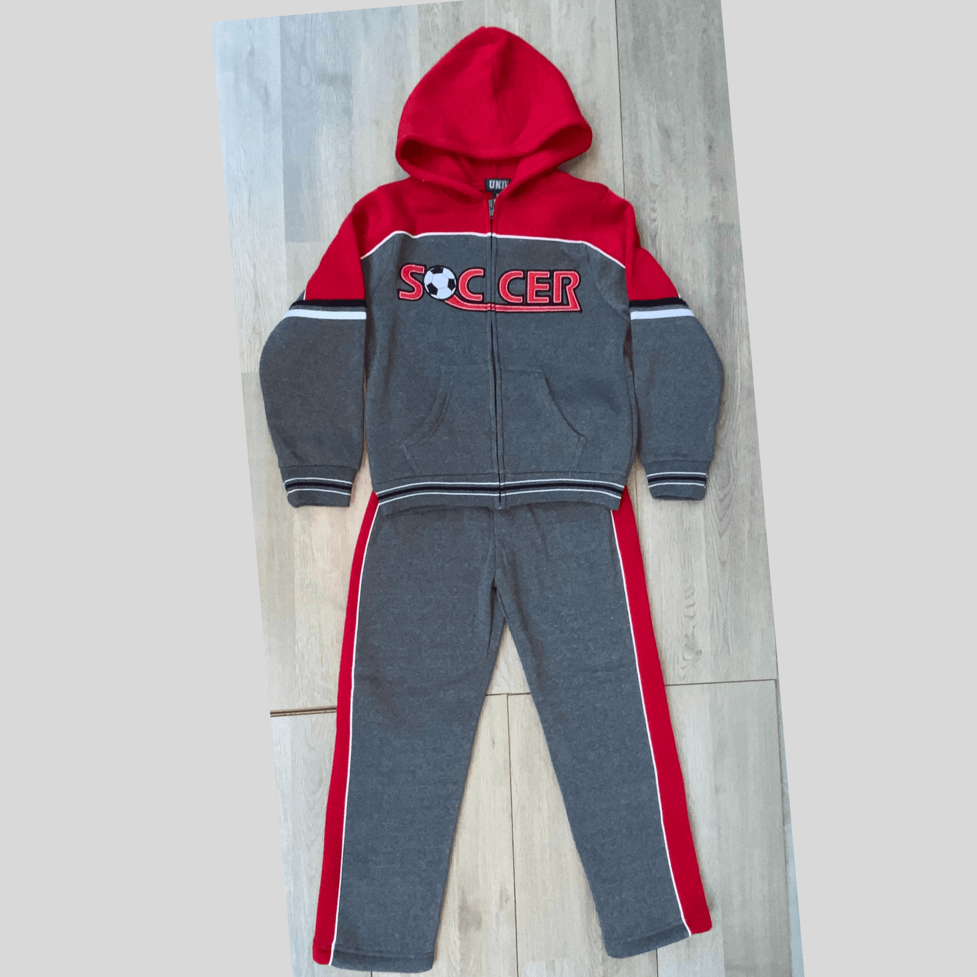 This dark grey soccer fleece set is perfect for your little soccer fans.  This sweat suit features thick red stripes down the side of the legs and the word "Soccer" embroidered on the front of the hoodie with a soccer ball for the letter o.